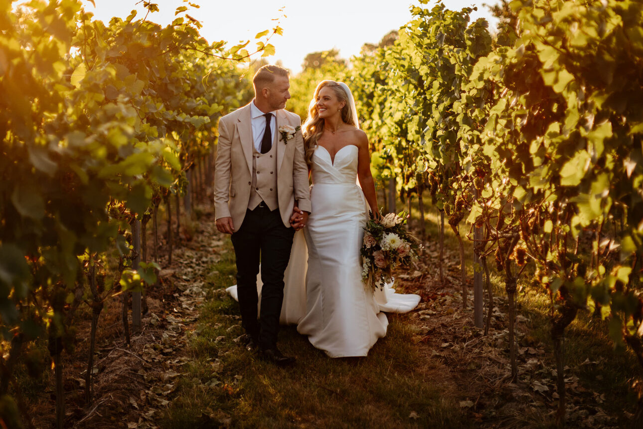 A bride and groom holding hands and walking through the vineyard at High House weddings 