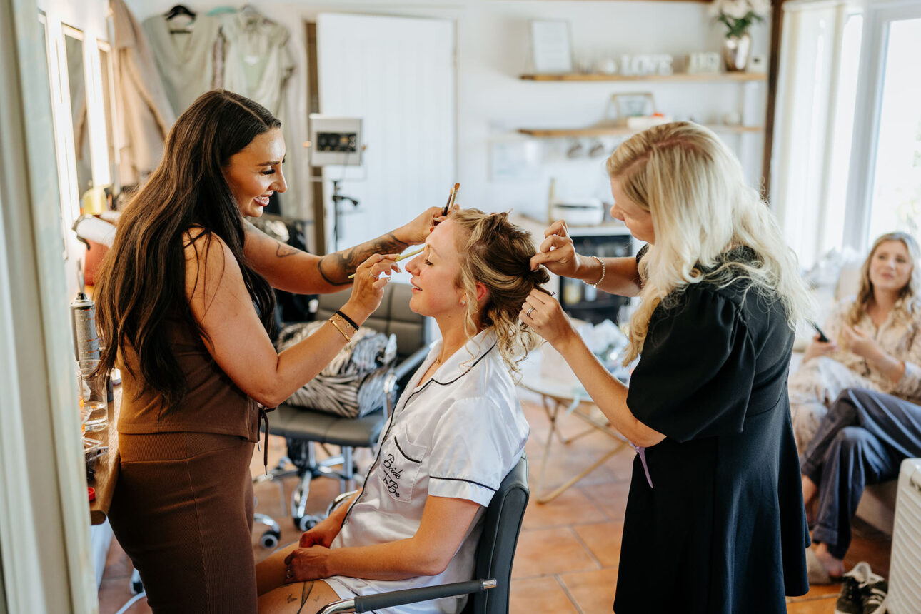 An interior photo in the dressing room at High House weddings, taken on a wedding morning and showing a bride having her hair and her makeup done at the same time. 