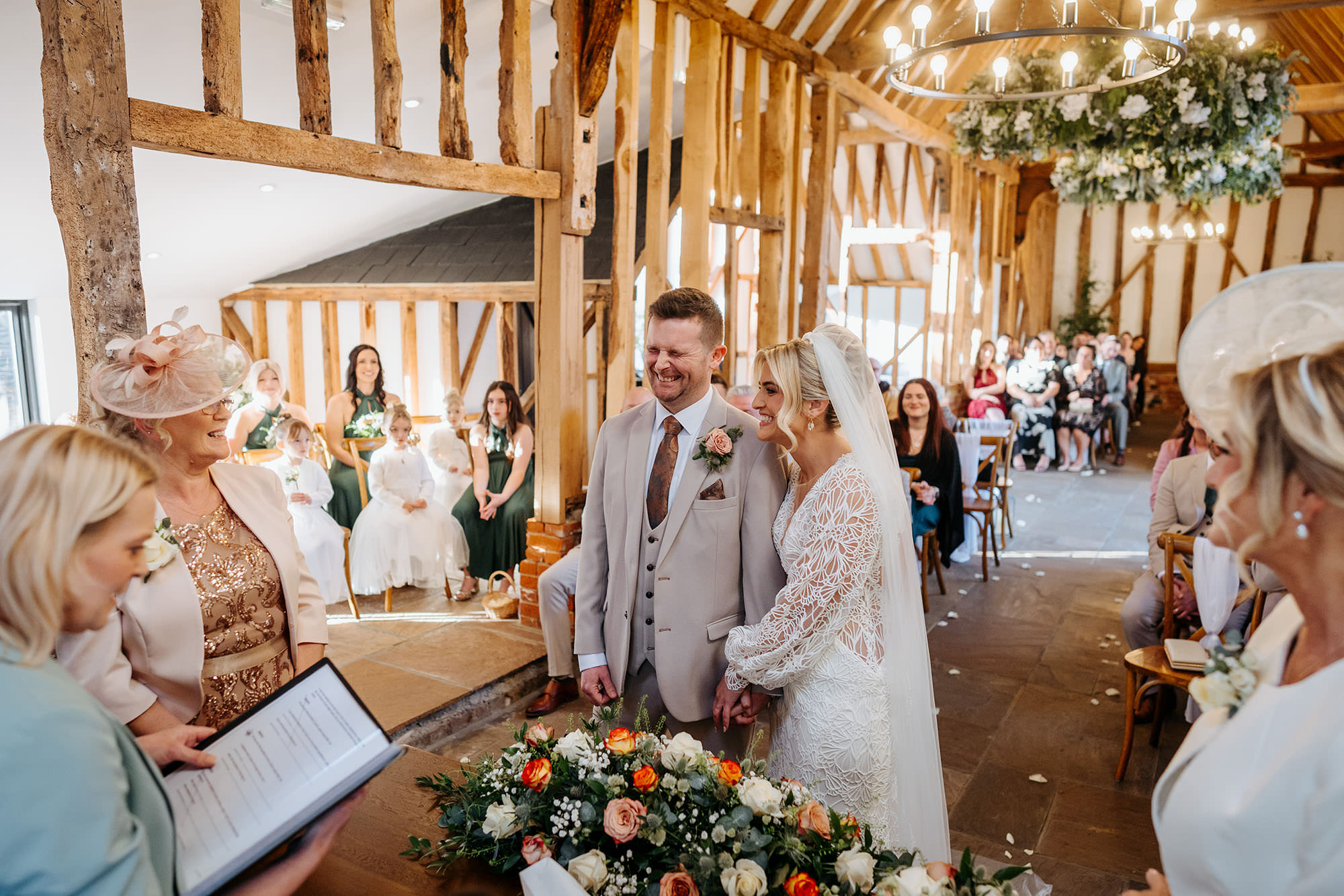 Couple getting married at High house Weddings inside the grade 2 listed barn. The couple are laughing and holding hands whilst their guests watch. 